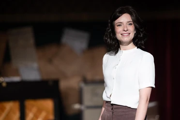 THE ARTIFICIAL SILK GIRL An actress in a white blouse smiles on a theater stage against a dark background