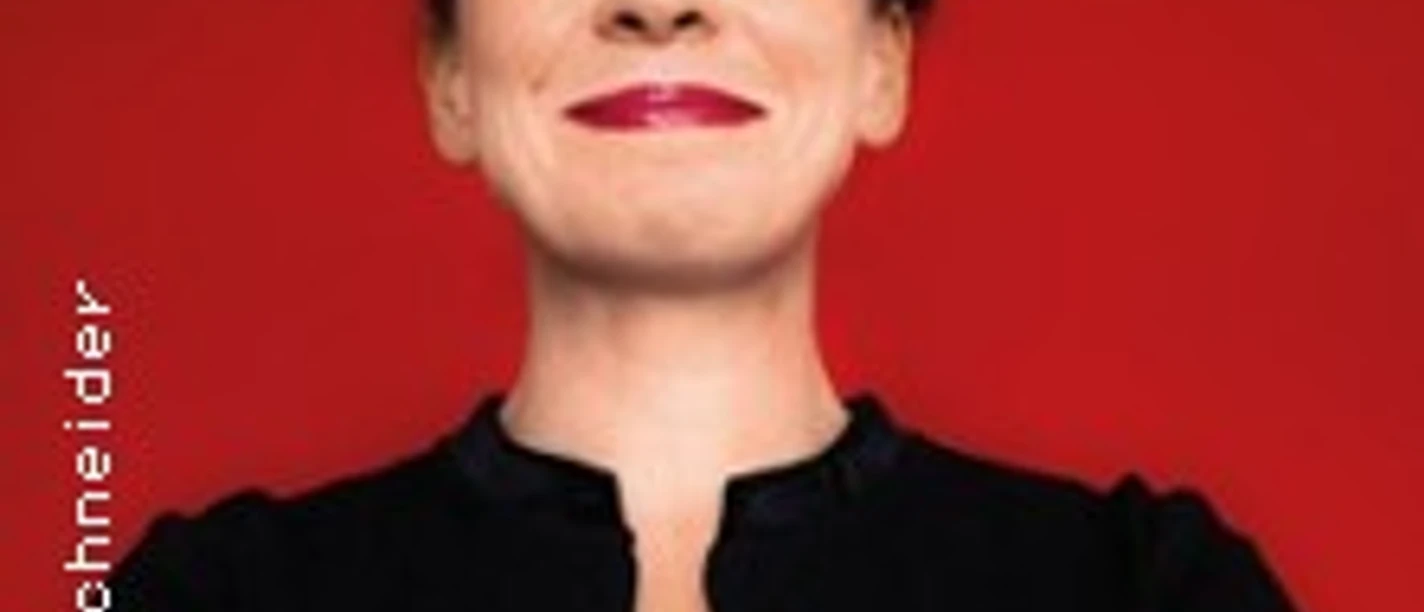 Tina Teubner vor rotem Hintergrund, in schwarzer Kleidung mit verschränkten Armen