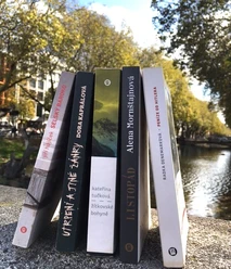 Es ist ein heller Sommertag. Fünf Buchrücken sind erkennbar. Die Bücher stehen auf einer der Brücken, die beide Straßenseiten der Königsallee in Düsseldorf mit ihren großen Platanen verbinden.