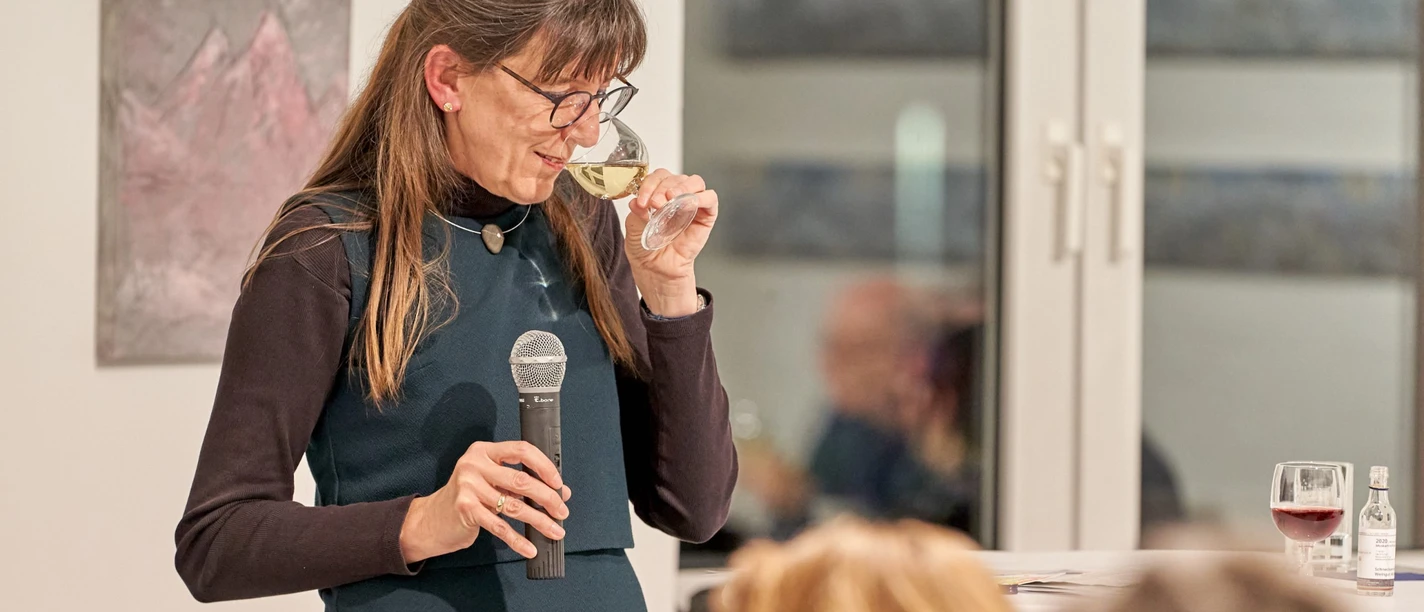 Eine Frau mit dunklen langen Haaren riecht an einem Glas Weisswein bei einer Weinprobe.