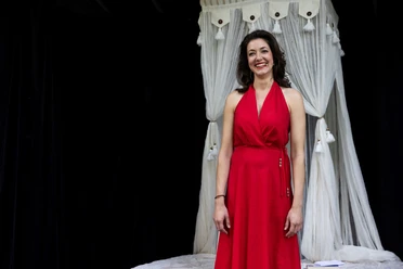 DAS LÄCHELN DER FRAUEN – Komödie von Nicolas Barreau Lachende Schauspielerin im roten Kleid vor weißem Bühnenvorhang
