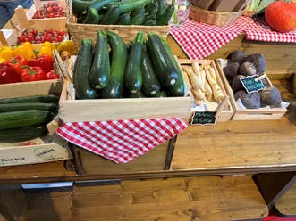 Uthmann_Hofladen_Gemueseangebot.jpg Gemüse in Kisten auf einem Holzregal. Zu sehen sind rote und gelbe Paprika, Zuchhine, rote Beete, Pastinaken.