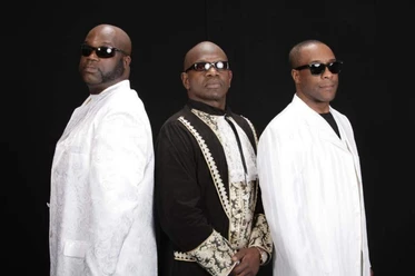 Charles Shaw & The Classic Brothers Three men dressed elegantly and wearing sunglasses are posing against a black background.