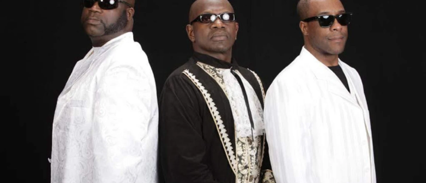 Charles Shaw & The Classic Brothers Drei Männer in eleganter Kleidung und Sonnenbrillen posieren vor schwarzem Hintergrund.