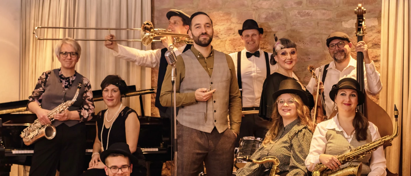 A jazz band dressed in elegant attire poses with their instruments in front of a stone backdrop.