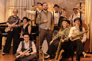 Salonorchester El´Sava Eine Jazzband in eleganter Kleidung posiert mit Instrumenten vor einem steinernen Hintergrund.