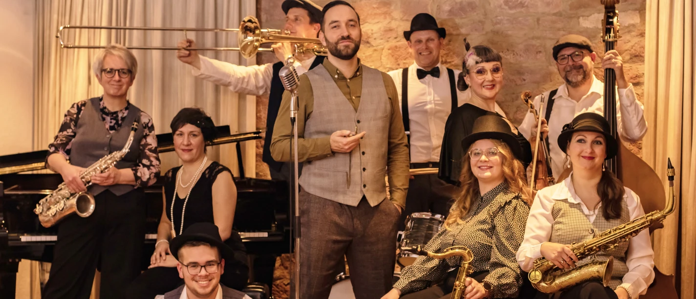 Salonorchester El´Sava Eine Jazzband in eleganter Kleidung posiert mit Instrumenten vor einem steinernen Hintergrund.