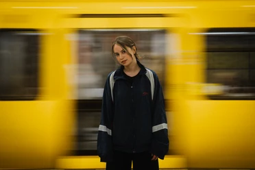 LILLI on the Frankfurt Music Stage A woman in an urban setting in front of a passing yellow subway train.