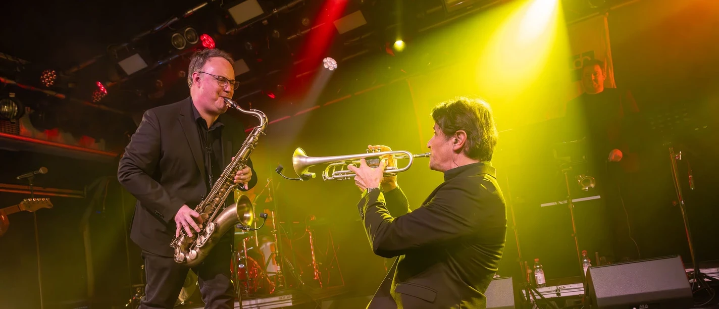 Soulfire Zwei Musiker spielen Saxophon und Trompete auf einer Bühne im bunten Licht.