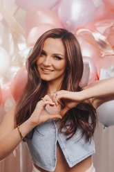 Amber van der Elzen Frau formt Herz mit Händen vor rosa und weißen Luftballons.