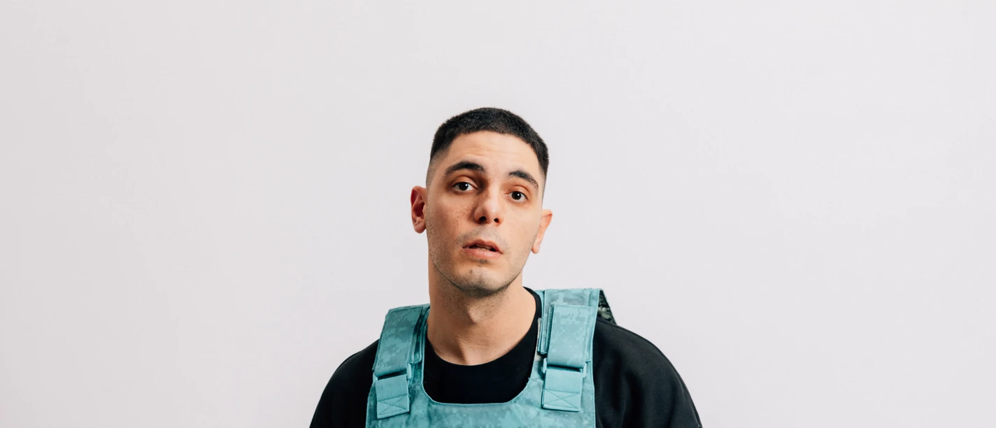 Nico Laska Mann in schwarzem Outfit trägt eine türkisfarbene Weste mit rotem Herzsymbol.