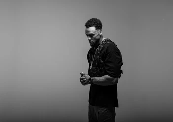 CA3SAR Black-and-white portrait of a pensive man in a black outfit against a gray background.