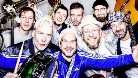 Gruppe von fröhlichen Männern mit Instrumenten und Hüten posiert für ein nahes Foto.