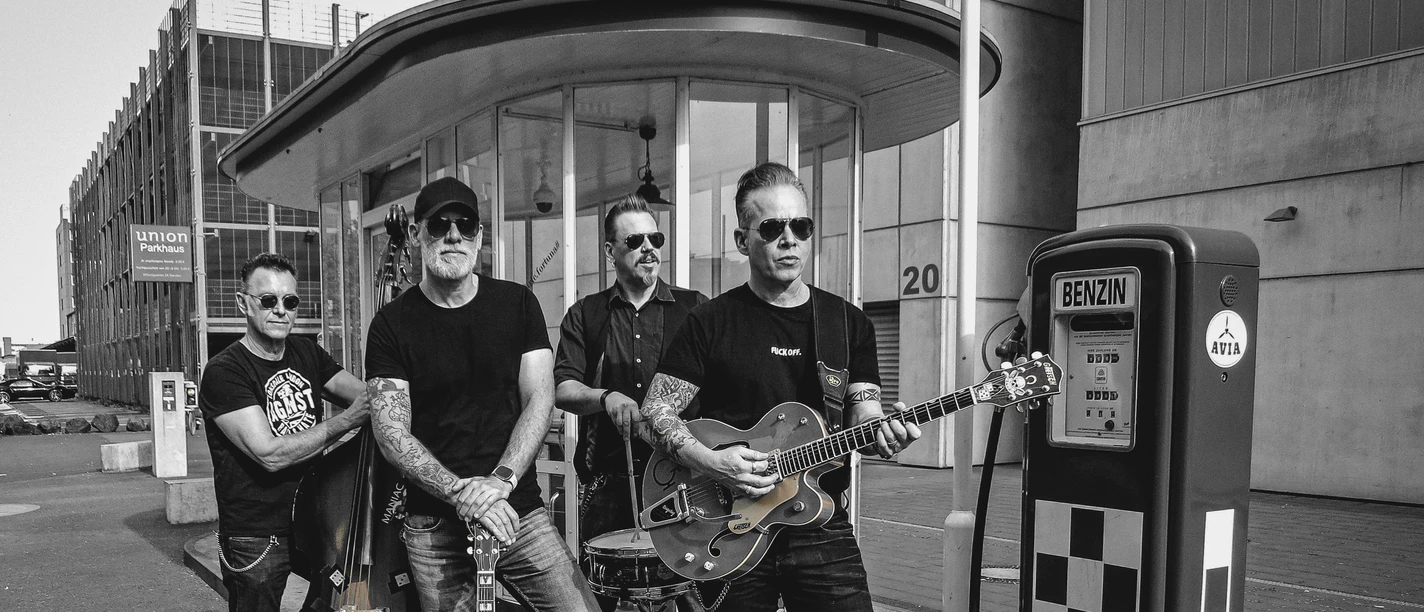 Frankfort Special Band posiert mit Instrumenten neben einer alten Benzinpumpe in schwarz-weiß.