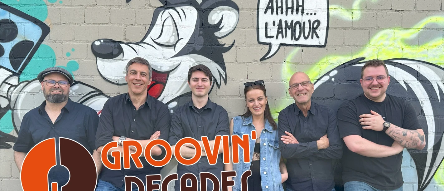 KULT-Net Bühne - GROOVIN´ DECADES Sechs Bandmitglieder lächeln vor einer Wand mit Cartoon-Graffiti