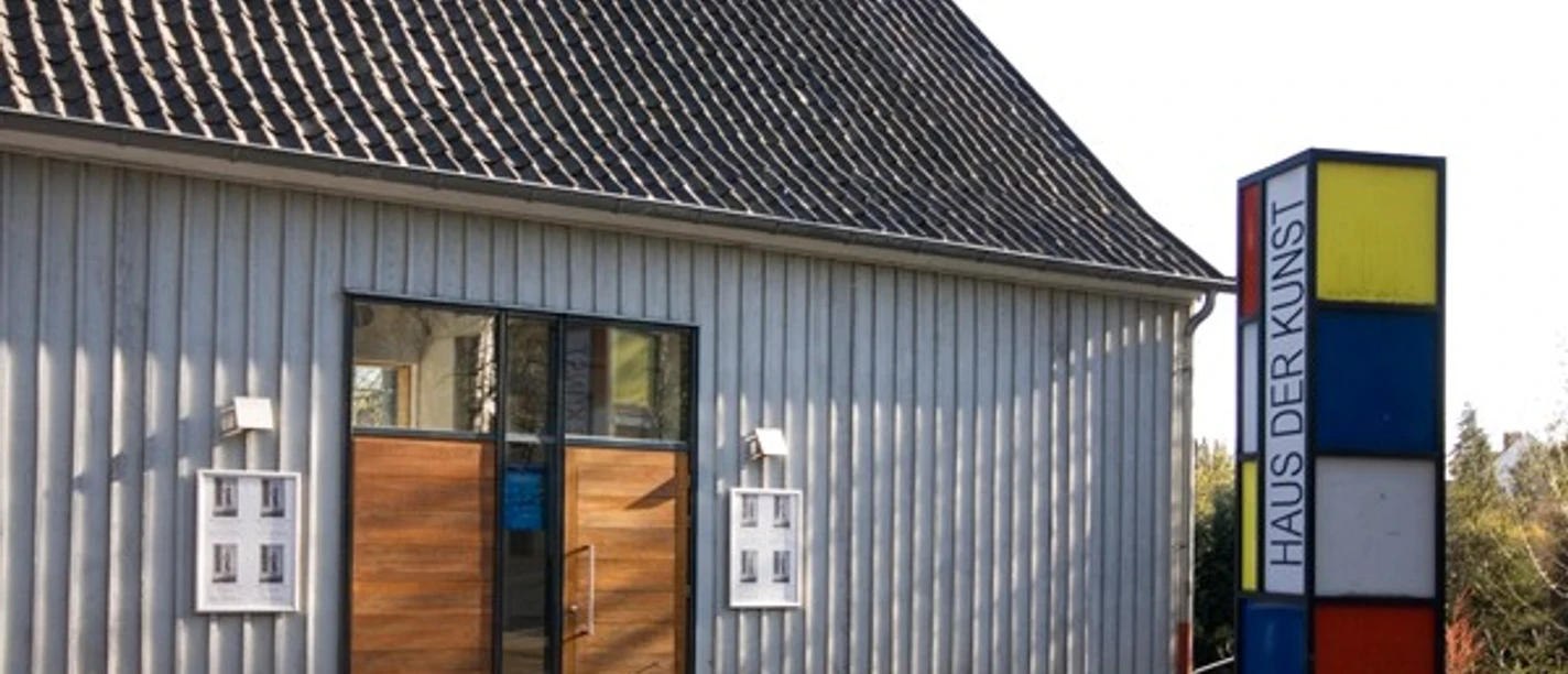 Eingang des Haus der Kunst in Nümbrecht mit Holzportal und farbiger Stele am Straßenrand