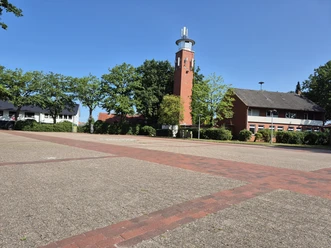 Gepflasterter Parkplatz am Marktplatz mit Bäumen, Wohnhäusern und hohem Backsteinturm.