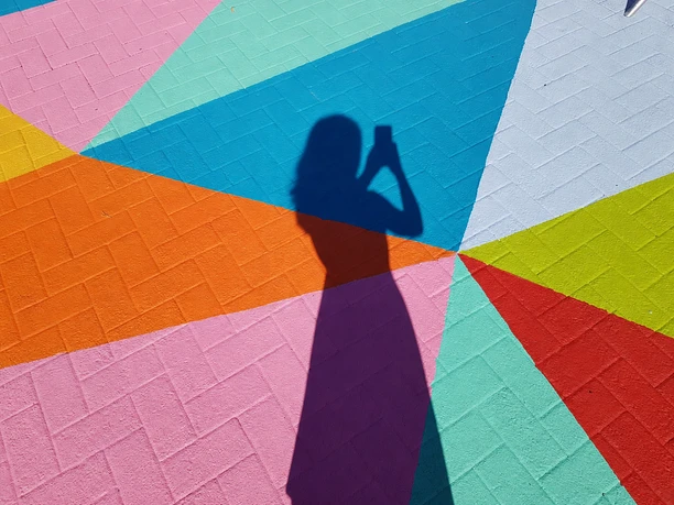Schatten einer Person mit Handy auf buntem Boden.