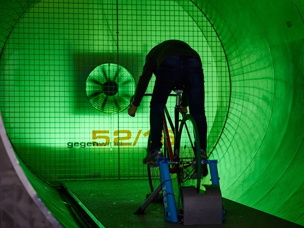 Deutsches Sport & Olympia Museum - Ausstellungsraum Person auf Rennrad-Simulator in grün beleuchtetem Windkanal des Sportmuseums