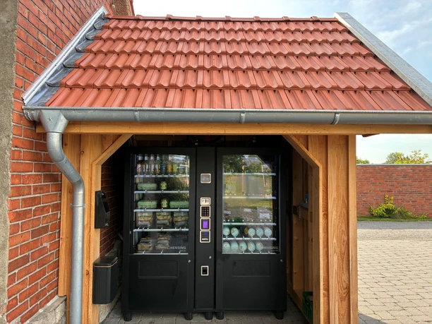 Zwei Verkaufsautomaten in einer Holzhütte mit roten Ziegeldach.