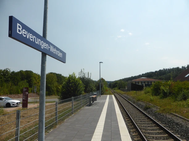 Linksseitig Parkmöglichkeiten, Schienenverlauf und blaues Schild mit weißem Schriftzug Beverungen-Wehrden