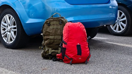 Two backpacks are resting on the ground next to a blue car in a parking lot during daytime. Travel concept