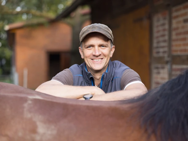 Olaf Böhne stützt mit Armen auf dem Rücken eines Pferdes