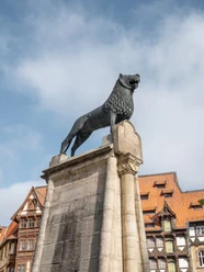 Braunschweiger Löwe auf steinernem Sockel vor Fachwerkhäusern am Burgplatz.