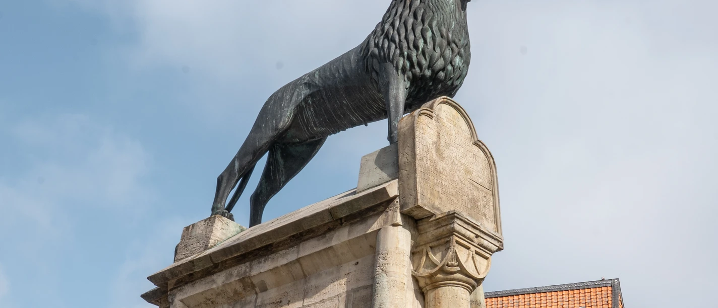 Braunschweiger Löwe auf steinernem Sockel vor Fachwerkhäusern am Burgplatz.