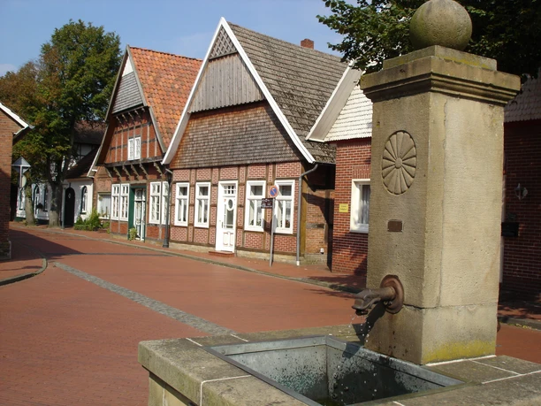 Fietsen op de Giebeltour in het Artland Bakstenen huizen aan een geplaveide straat met een fontein op de voorgrond in een typisch Nedersaksisch dorp.