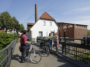 Radeln auf der DiVa-Tour Gruppe von Radfahrern auf einer Brücke bei einem historischen Gebäude aus rotem Backstein.