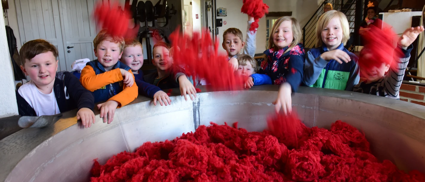 Een groep kinderen speelt met felrode katoenstapels in een industriële ruimte.