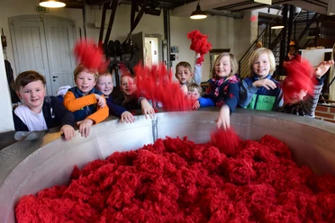 Im Tuchmachermuseum Bramsche A group of children play with bright red cotton pile in an industrial space.