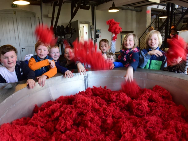 Eine Gruppe von Kindern spielt mit leuchtend rotem Baumwollflor in einem Industrieraum.
