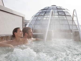 carpesol SPA Therme Paar entspannt im sprudelnden Außenpool mit Kuppelgebäude im Hintergrund.Couple relaxing in the bubbling outdoor pool with the domed building in the background.Et par slapper af i den boblende udendørs pool med den kuppelformede bygning i baggrunden.Een koppel ontspant in het borrelende buitenzwembad met het koepelvormige gebouw op de achtergrond.