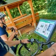 Hörstation auf der Ackerschnacker Tour Zwei Radfahrer betrachten eine Infotafel neben einem überdachten Holzunterstand im Grünen.Two cyclists look at an information board next to a covered wooden shelter in the countryside.To cyklister kigger på en informationstavle ved siden af et overdækket træskur på landet.Twee fietsers kijken naar een informatiebord naast een overdekt houten afdak op het platteland.