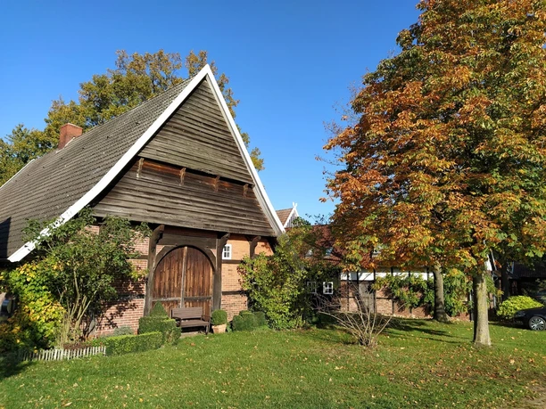 Hofanlage Historischer Bauernhof mit Fachwerk, umgeben von Bäumen im Herbst auf einem sonnigen Tag.