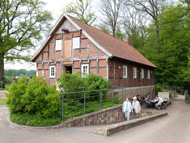 Heimathaus Bersenbrück Fachwerkhaus aus Backstein in ländlicher Umgebung mit parkenden Menschen und grüner Vegetation.