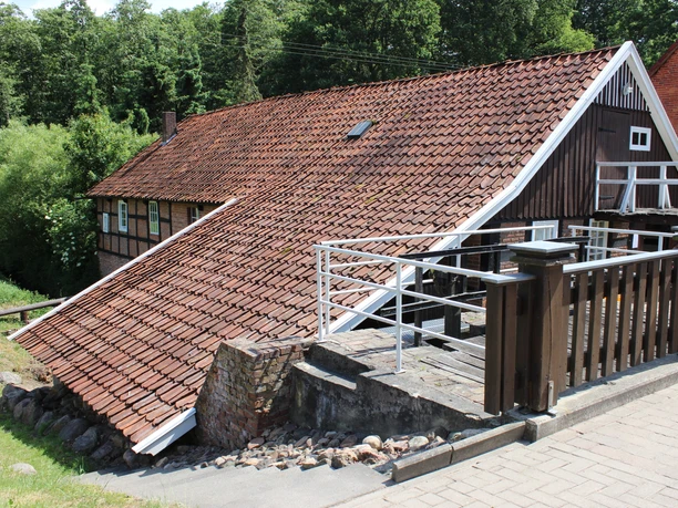 Alte Wassermühle Rotes Ziegeldach eines Fachwerkhauses in einer grünen, bewaldeten Umgebung.