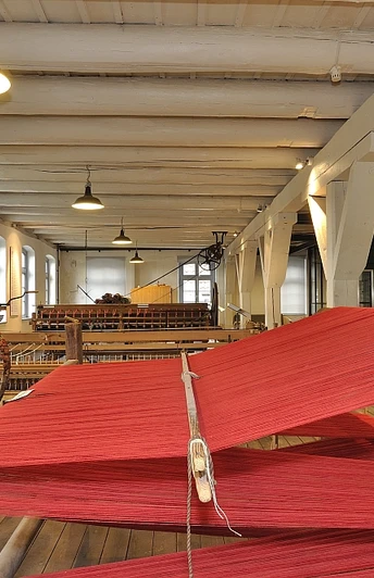 Radeln auf der der Route Bramsche 2 Historische Weberei mit roten Fäden auf hölzernem Gestell in lichtdurchflutetem Raum.Historic weaving mill with red threads on a wooden frame in a light-flooded room.Historisk væveri med røde tråde på en træramme i et lysgennemstrømmet rum.Historische weverij met rode draden op een houten frame in een lichtovergoten kamer.