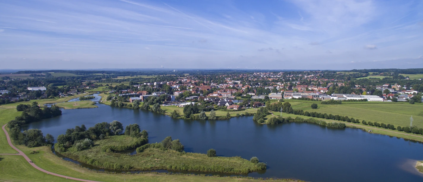 Radeln auf der der Route Bramsche 2 Luftaufnahme eines Sees inmitten einer Landschaft mit einer Stadt im Hintergrund.
