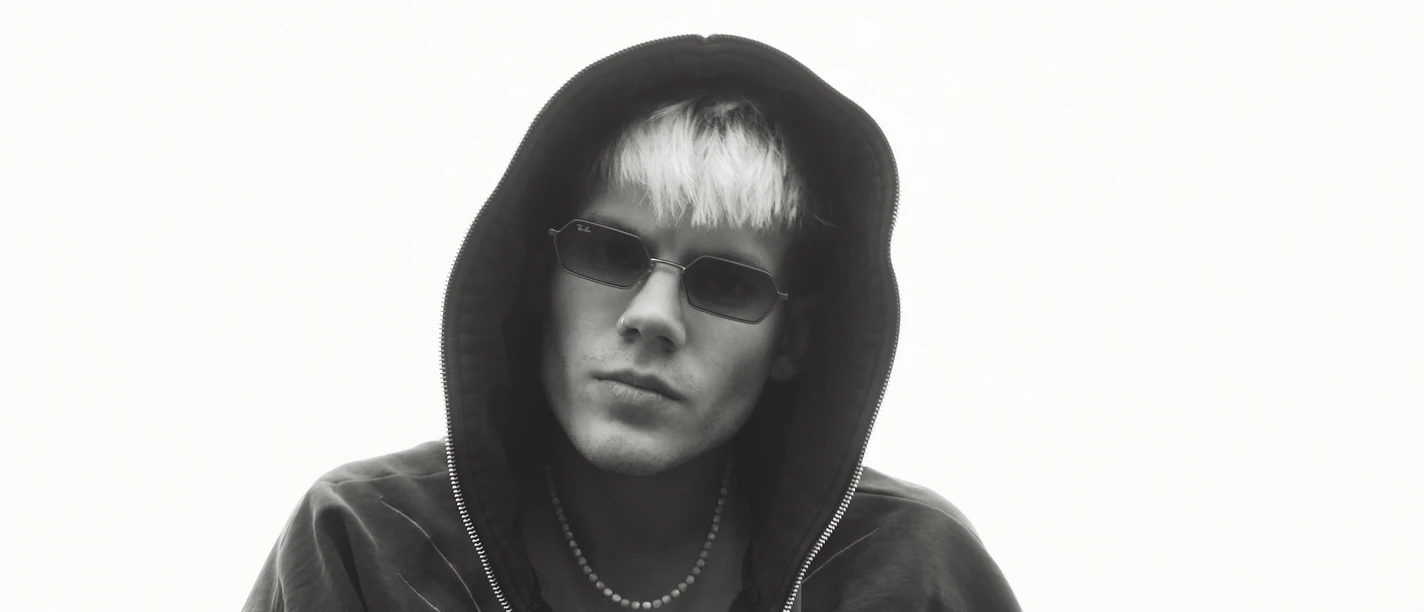 Person mit Kapuzenjacke und Sonnenbrille vor hellem Hintergrund