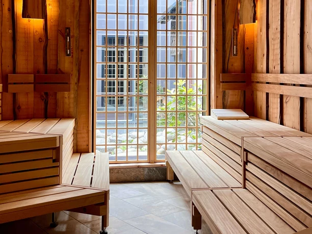 Holzverkleidete Aufgusssauna mit Liegebänken, warmem Licht und Fenster zum Innenhof