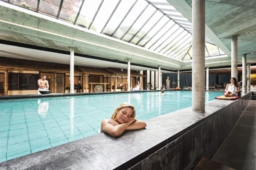 Neptunbad - Indoor Sentō Bath Indoor pool at Cologne's Neptunbad, featuring a glass roof, columns, and relaxed guests at the poolside