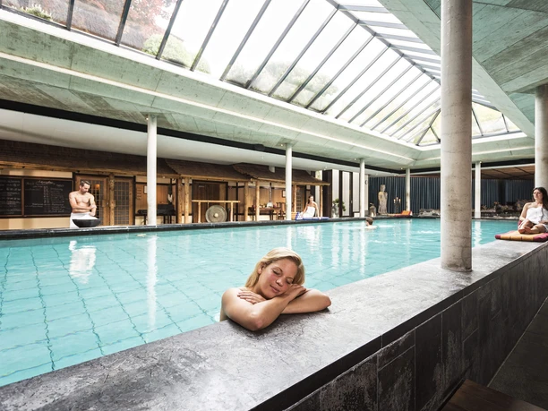 Innenpool im Kölner Neptunbad mit Glasdach, Säulen und entspannten Gästen am Beckenrand