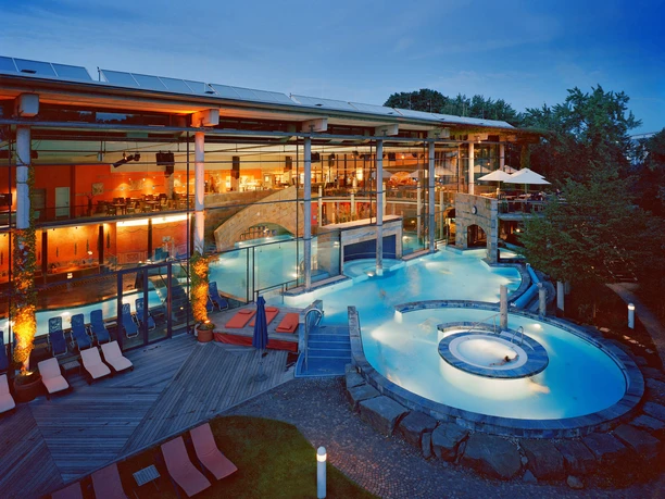Abendansicht der Claudius Therme mit beleuchteten Thermalbecken und Liegen