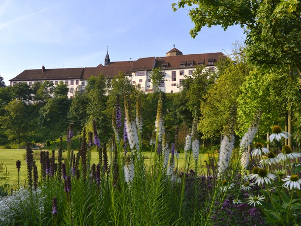 Historisch kasteel omringd door weelderige tuinen, zomerbloesems op de voorgrond.