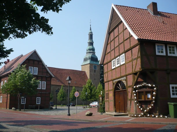 Artländer Fachwerkgiebelmeile Fachwerkhäuser mit dekoriertem Eingang, Turm im Hintergrund, blauer Himmel.