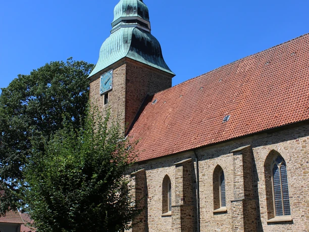 Radeln auf der Artländer Fachwerkgiebelmeile Historische Kirche aus Backstein mit hohem Turm und grünlicher Turmspitze bei blauem Himmel.