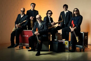 The Blues Company und Fabulous BC Horns mit Instrumenten in schwarzen Anzügen.